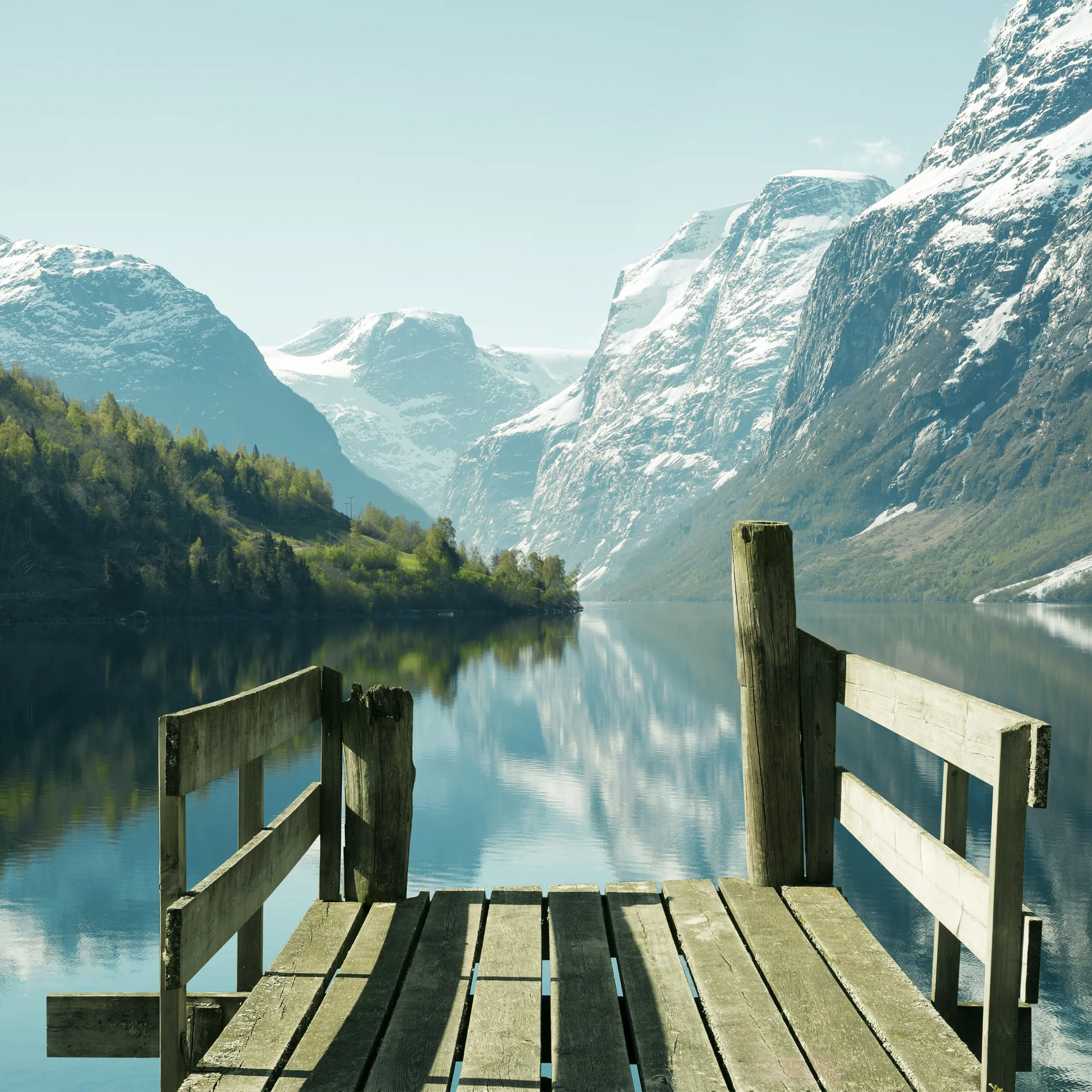 Liten trebrygge ut mot praktfullt norsk fjordlandskap, blå himmel.